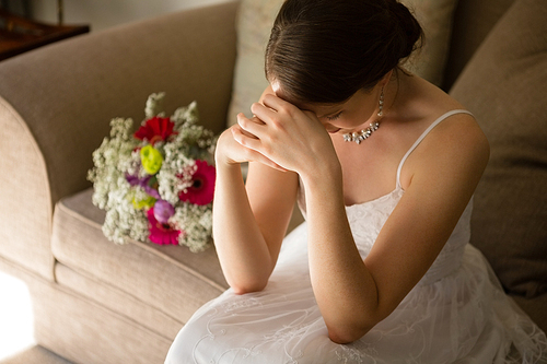 High angle view of upset bride sitting by bouquet on sofa at home