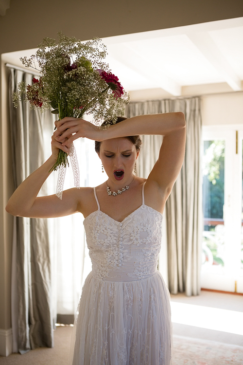 Angry bride throwing bouquet while standing at home