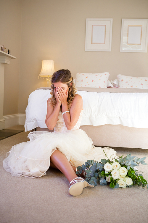 Bride in wedding dress crying while sitting by bed at home