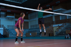 Full length of woman looking at male teammate jumping at volleyball court
