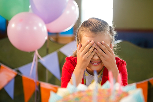 Cute girl covering her eyes during birthday party at home