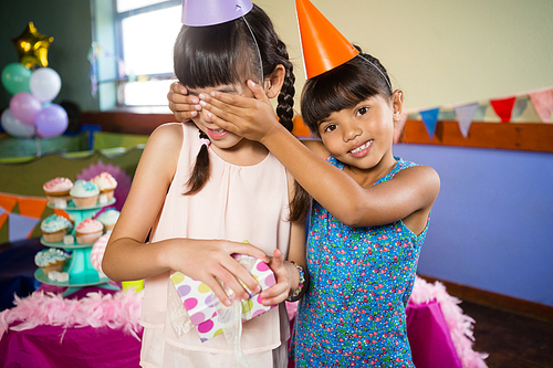 Smiling girl covering birthday girls eyes and offering a gift