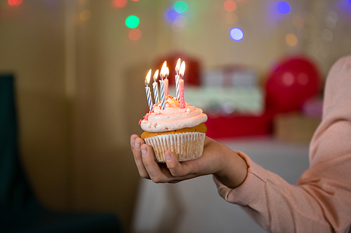 Girl holding cupcake with lit candle during birthday party at home