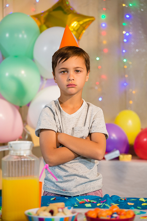 Portrait of cute boy standing with arms crossed at birthday party