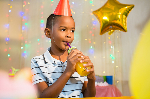 Thoughtful boy drinking juice during birthday party at home