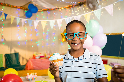 Portrait of cute boy holding cupcake during birthday party at home