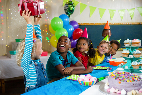 Children looking at girl holding gift during birthday party