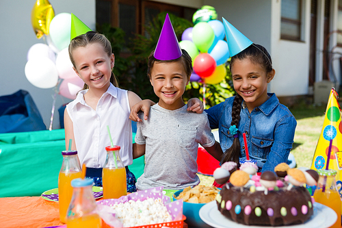 Portrait of children sitting at table during birthday party in yard
