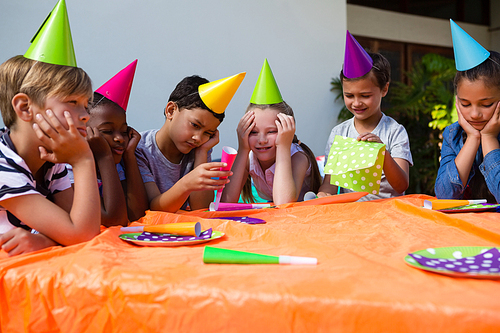 Bored children sittng at table in yard during birthday party