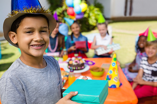Portrait of boy showing gift box with friends in background