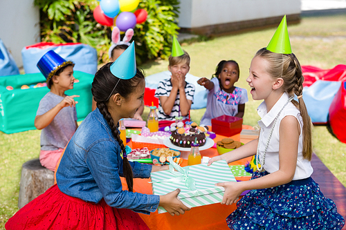 Friend giving gift to girl during birthday party in yard