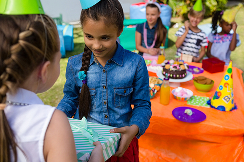 Girl giving gift to friend during birthday party in yard
