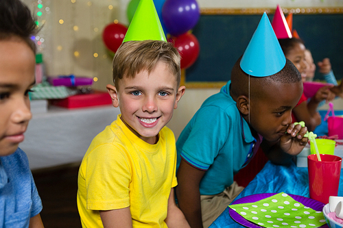 Portrait of boy sitting by friends at table during birthday party