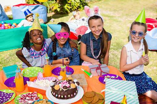 Portrait of female friends sitting at table in yard during birthday party