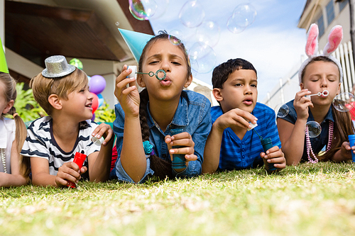 Children blowing bubbles while lying on field in yard