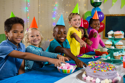 Portrait of children pointing on cake during birthday party