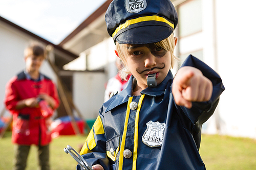 Portrait of boy in police costume gesturing while standing in yard