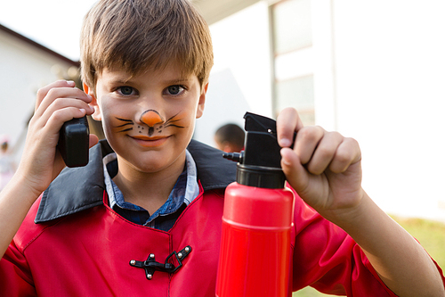 Portrait of boy with face paint using walkie talkie while holding fire extinguisher during birthday party