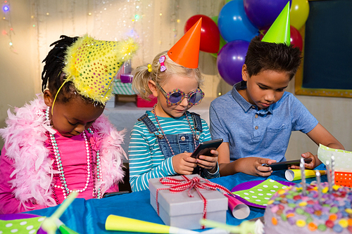 Children using mobile phone while sitting at table during birthday party