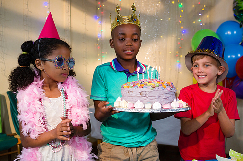 Children looking at cake held by boy during birthday party