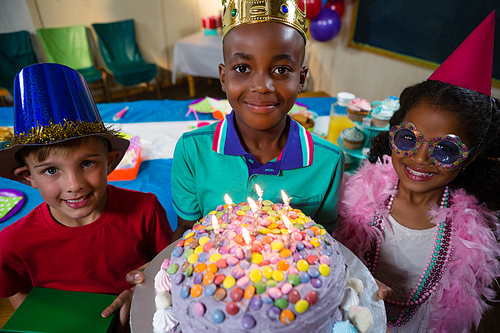 High angle portrait of boy holding birthday cake while standing with friends