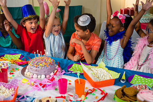 Cheerful children with arms raised sitting at table during birthday party