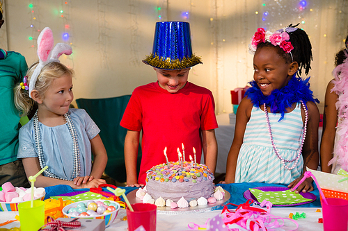 Friends looking at boy standing by cake during party