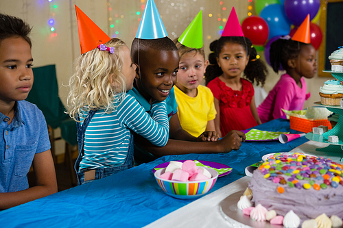 Girl whispering to boy at table during birthday party