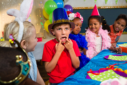 Boy making face while sitting with friends at table during birthday party