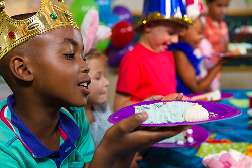 Close up of boy looking at cake in plate while sitting with friends