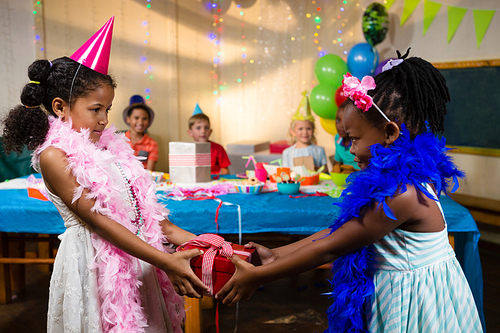 Side view of girl giving gift to friend during birthday party