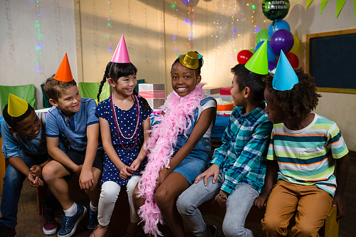 Happy children sitting against wall during birthday party