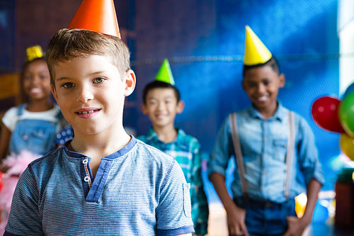 Portrait of boy wearing party hand with friends in background during birthday party