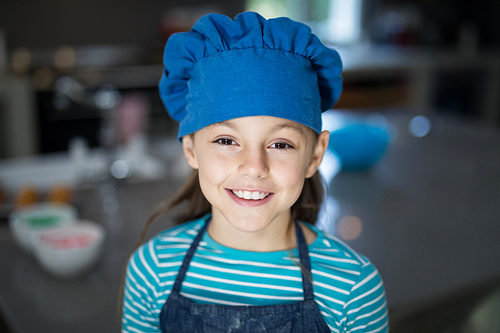 Close-up of smiling girl wearing an apron and a cap in the kitchen