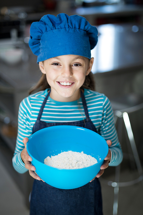 Close-up of smiling girl holding a bowl of flour in the kitchen