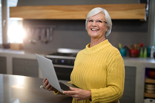 Senior women holding laptop while standing in the kitchen