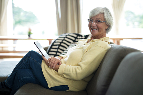 Portrait of smiling senior woman using digital tablet on sofa in living room