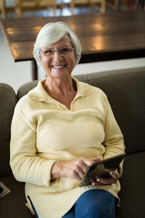 Portrait of smiling senior woman using digital tablet on sofa in living room