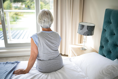 Rear view of senior woman sitting on bed in bedroom