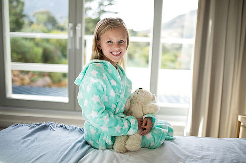 Portrait of smiling girl holding teddy bear on bed in bedroom