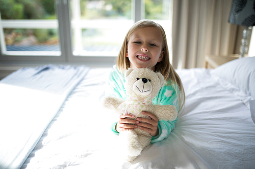 Portrait of smiling girl holding teddy bear on bed in bedroom