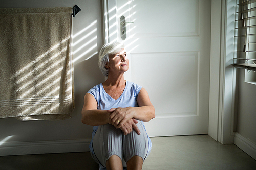 Tense senior woman looking through window in bedroom