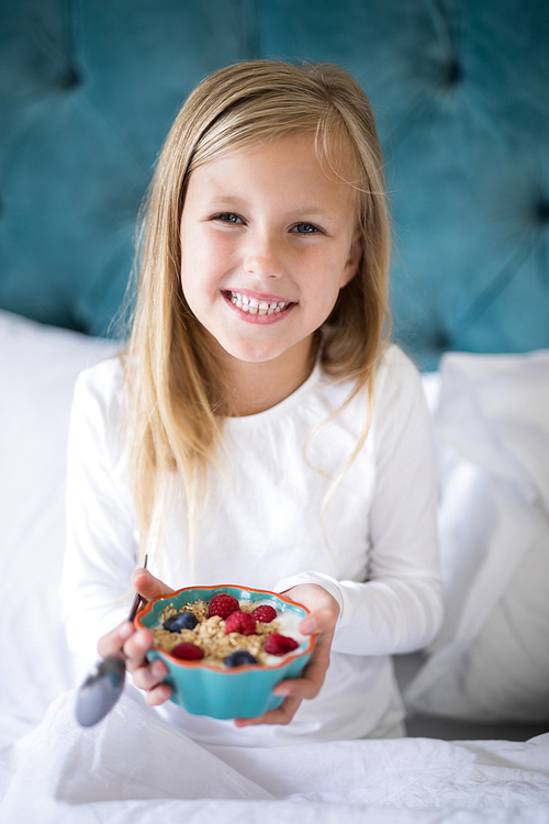 Portrait of smiling girl holding breakfast cereal on bed