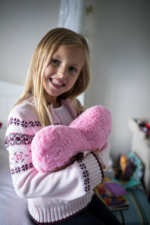 Portrait of smiling girl holding heart shape pillow on bed in bedroom