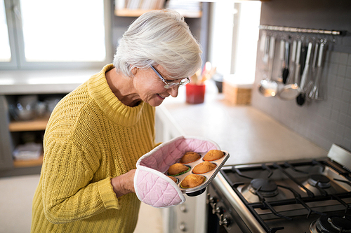 Smiling senior women holding freshly baked muffins wearing oven gloves