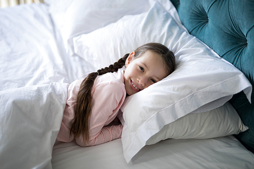 Portrait of smiling girl lying on bed in bedroom