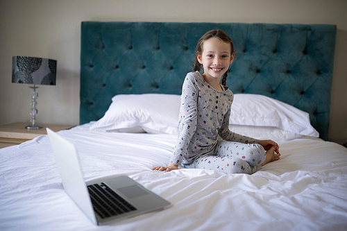 Portrait of smiling girl sitting on bed in bedroom
