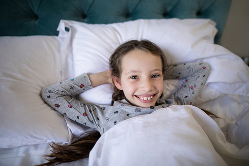 Portrait of smiling girl lying on bed in bedroom