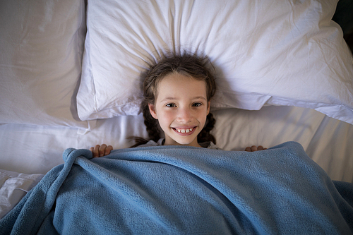 Portrait of smiling girl lying on bed in bedroom