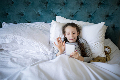 Smiling girl video calling on mobile phone in bedroom